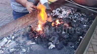 一个男人在烧烤时用热煤<strong>吹吹</strong>风。 在露天煮肉。 烧烤生活袋概念